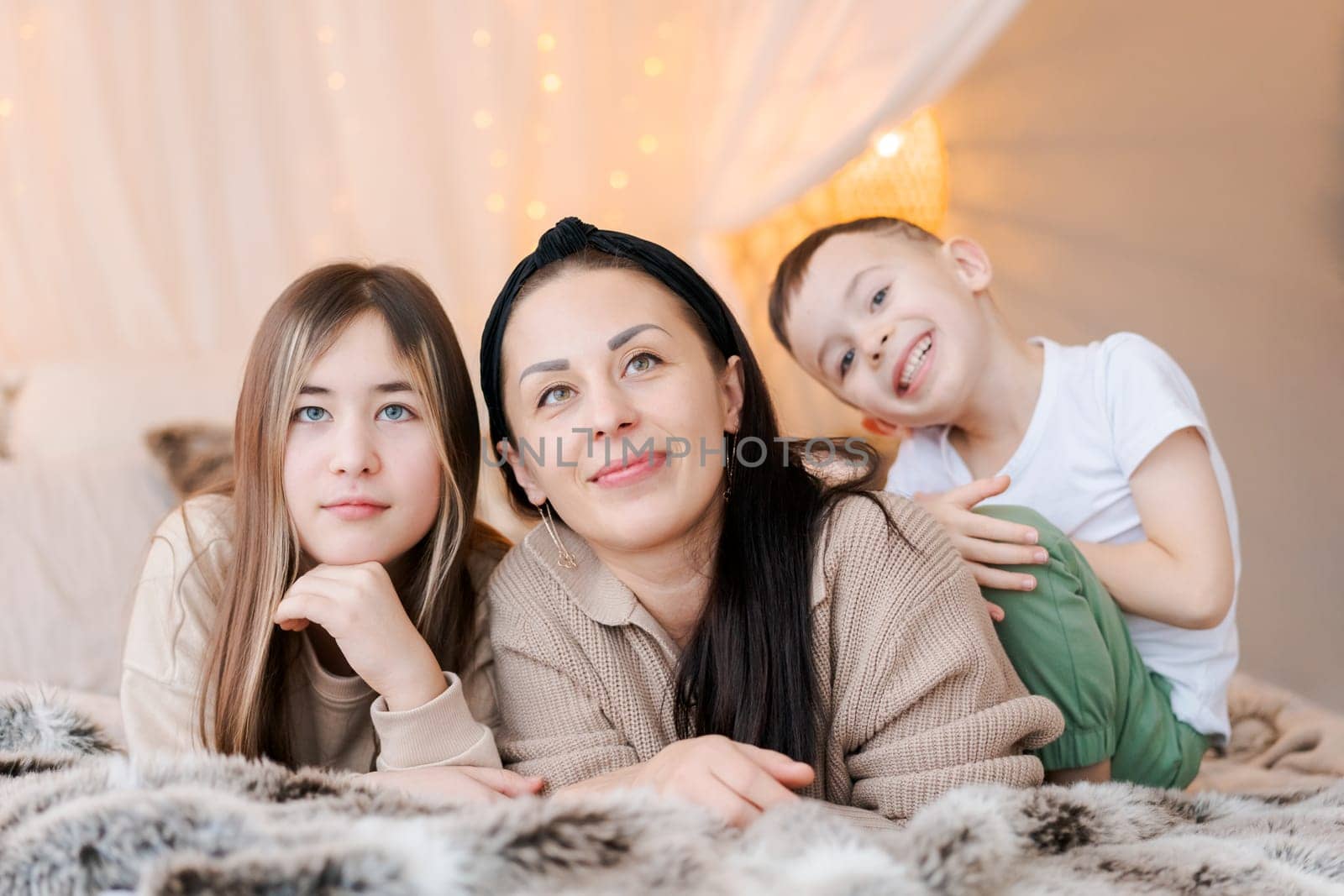 Mom and kids lying on bed in decorated bedroom and laughing concept winter by EkaterinaPereslavtseva