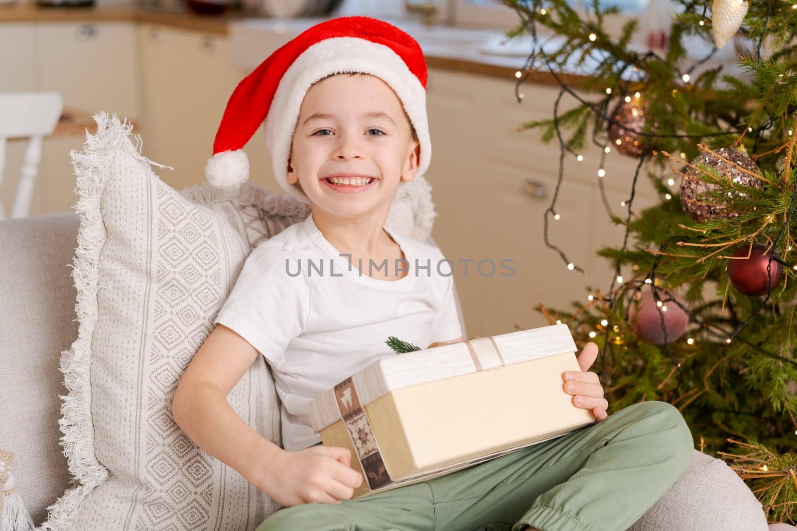 Cute little boy in Santa hat sits on couch with Christmas present from his family