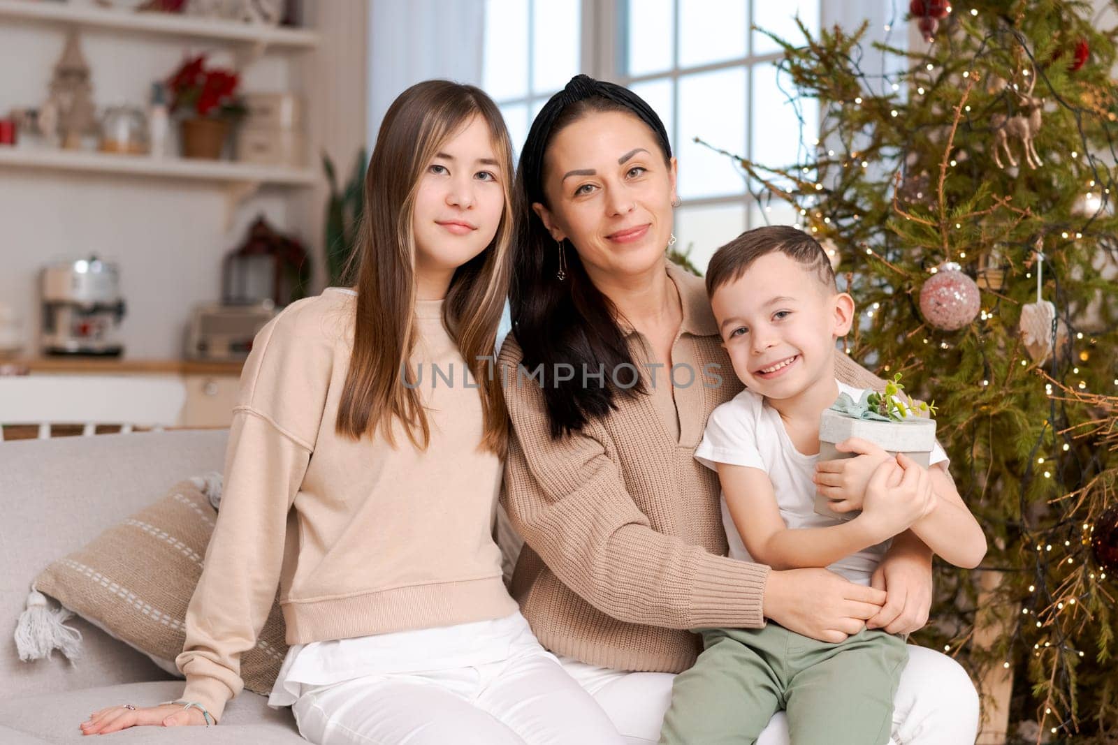 Family spends time together during Christmas holidays in decorated house. Mother and her two children hug each other as they prepare for holiday. Selective focus