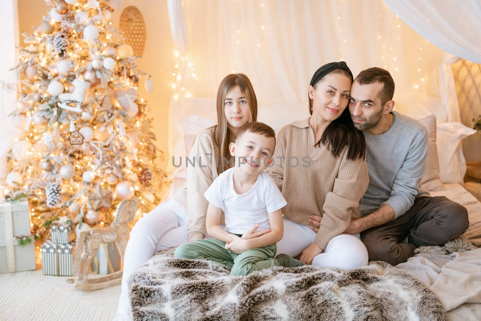 Happy family children and parents on bed in decorated bedroom at Christmas waiting for the holiday and laughing