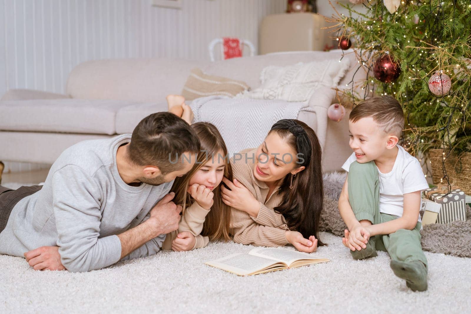 Happy family in decorated house at christmas lying on floor reading book by EkaterinaPereslavtseva