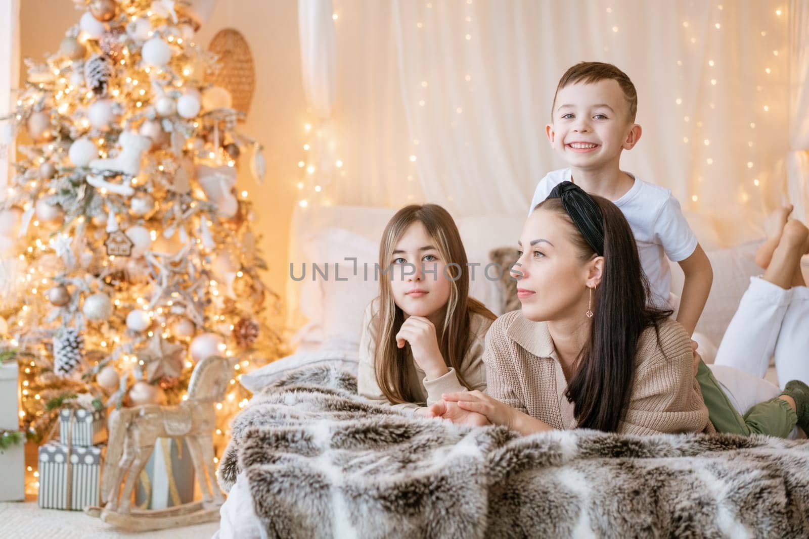 Happy family mom and two kids lying on bed waiting for Christmas and laughing