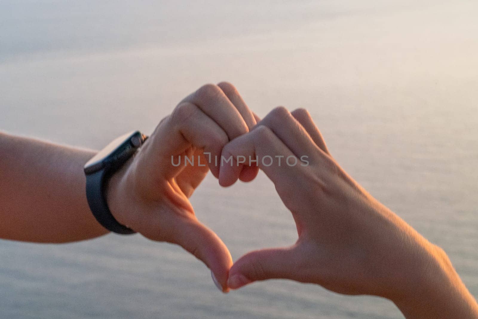 Hands heart sea sanset. Hands forming a heart shape made against the sun sky of a sunrise or sunset on a beach by Matiunina