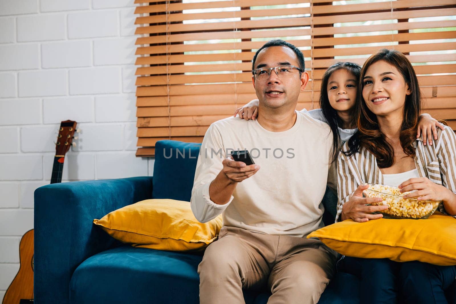 A joyful family spends quality time at home watching TV with popcorn on sofa. father mother son daughter and schoolgirl create precious family moments filled with candid enjoyment and happiness.