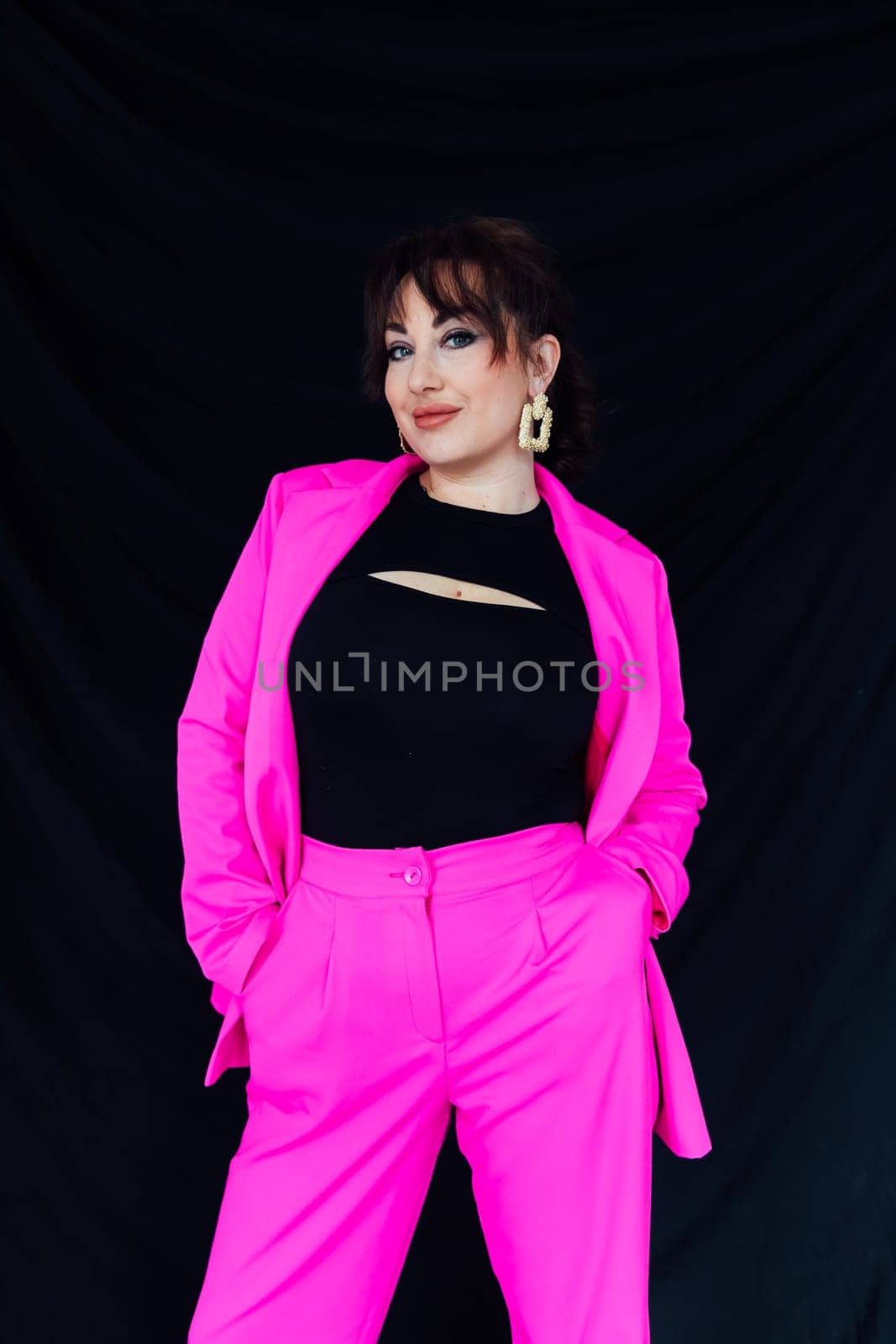 Woman in bright suit posing on black background in studio