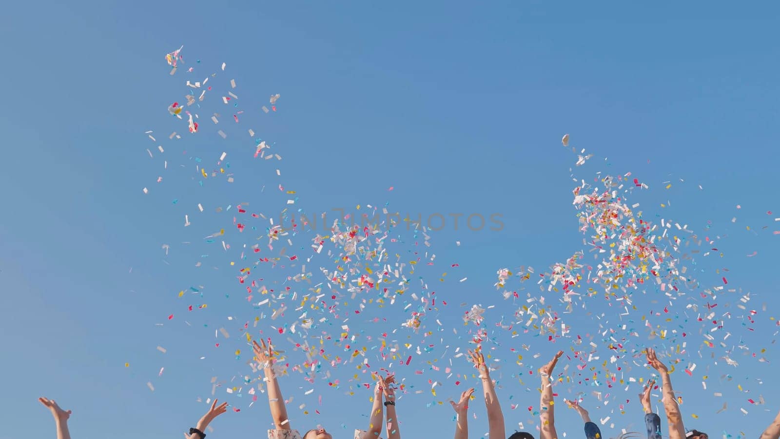 Tossing colorful paper confetti from the hands of young people. by DovidPro