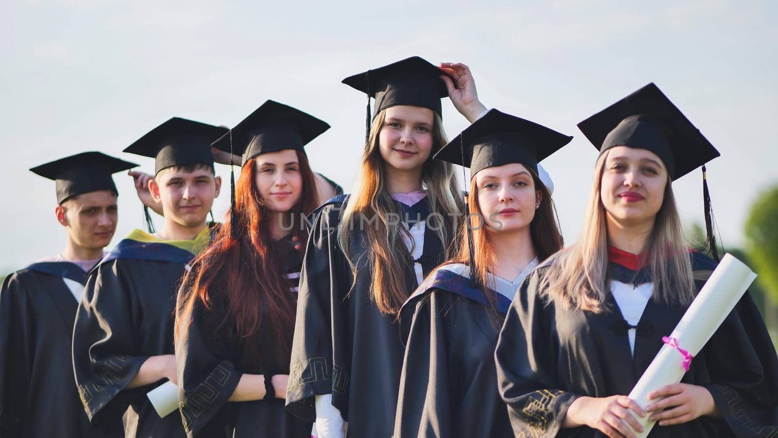 Cheerful graduates pose with raised diplomas on a sunny day. by DovidPro