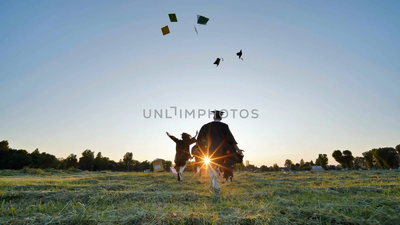 Cheerful graduates students run throwing notebooks after school at sunset