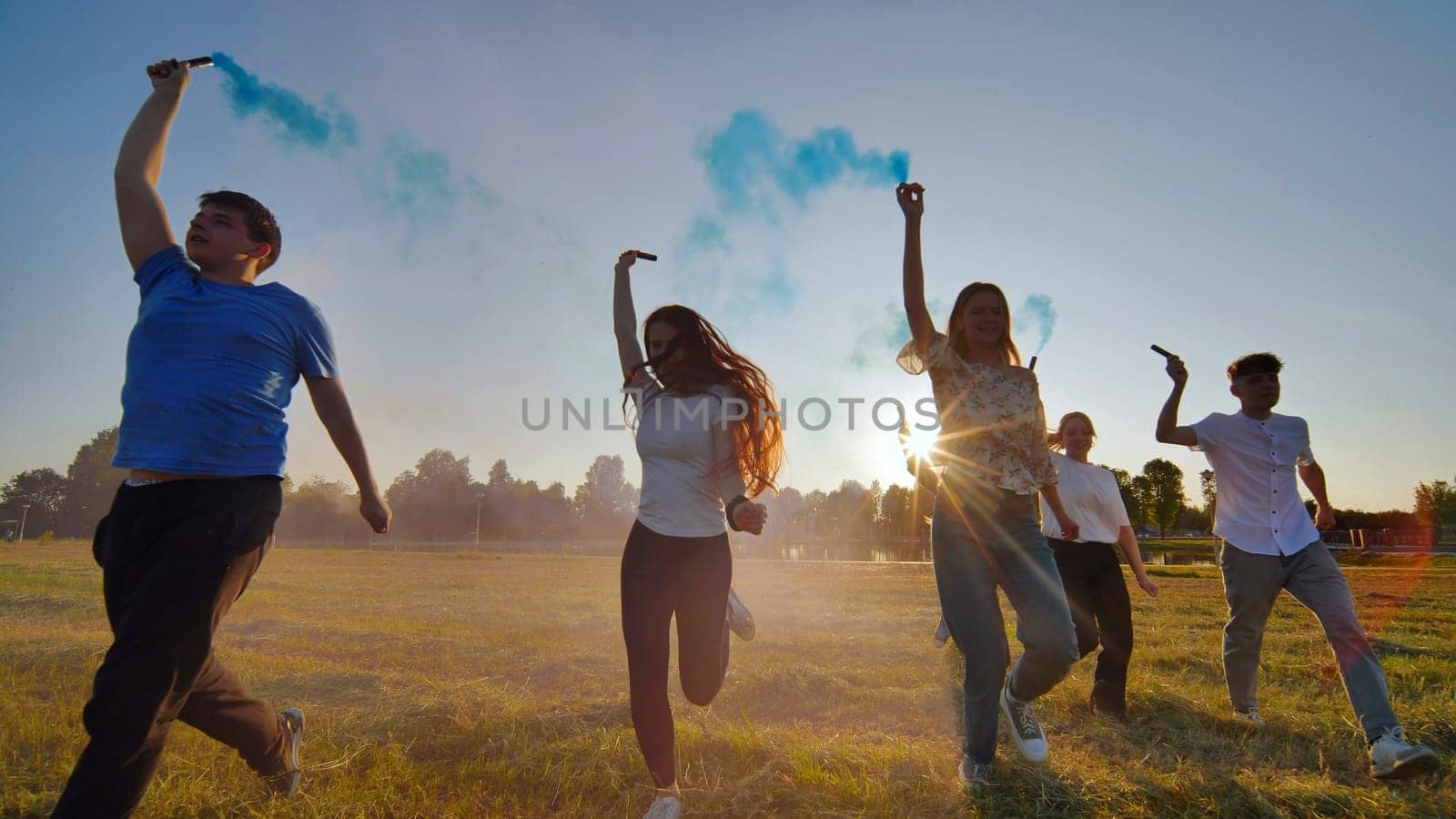 A group of friends spraying multi-colored smoke at sunset. by DovidPro