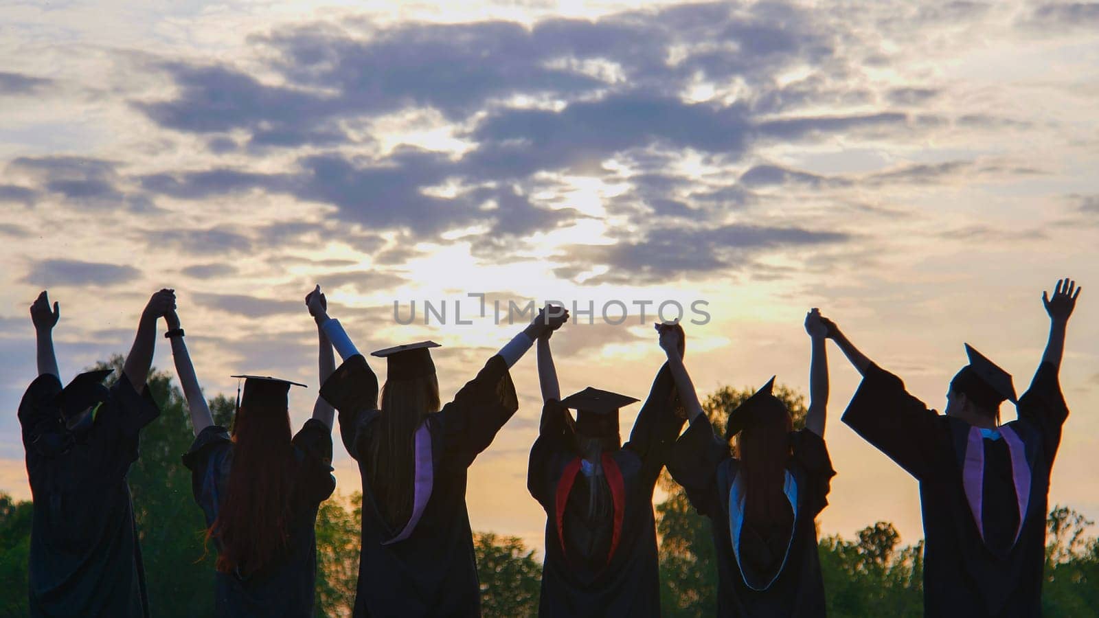 Silhouettes of graduates in suits at sunset waving to the sun. by DovidPro