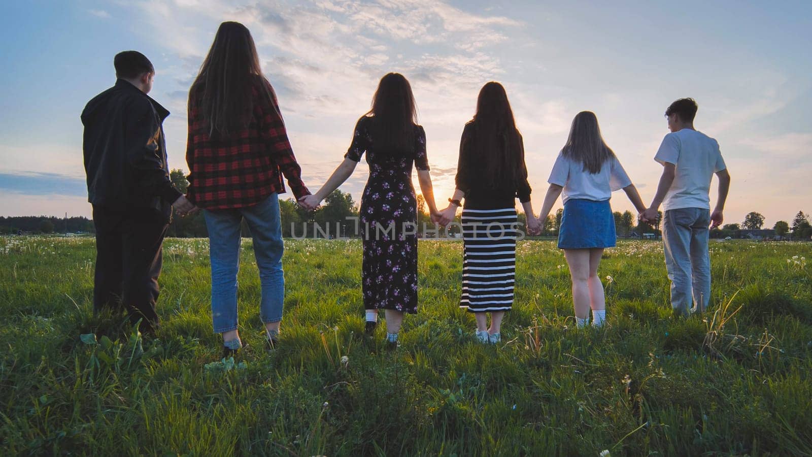 A group of friends stand in a row at sunset