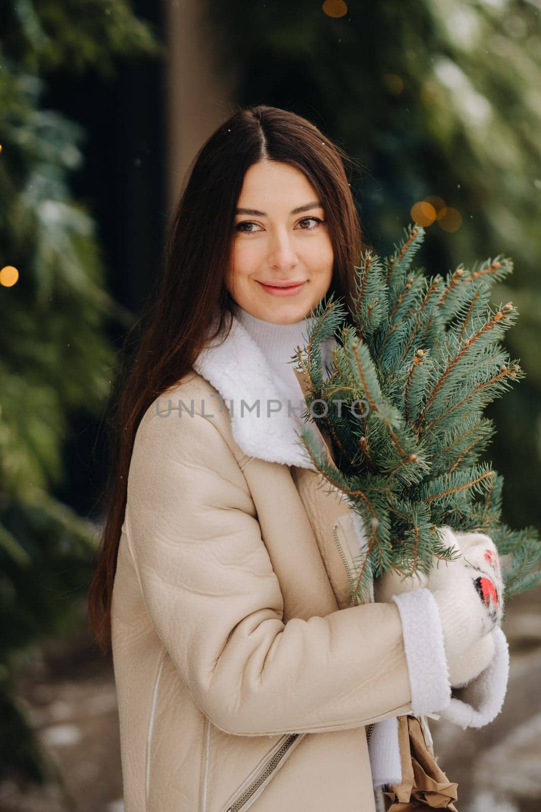 A girl with long hair in winter on the street with a bouquet of fresh fir branches.