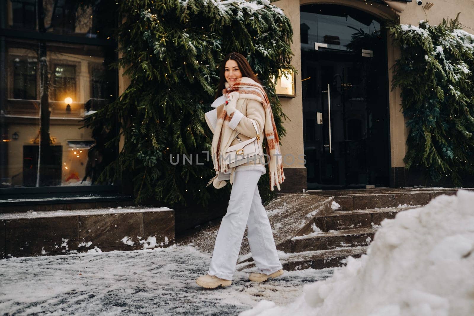A girl with long hair in a scarf and with a white handbag walks down the street in winter by Lobachad