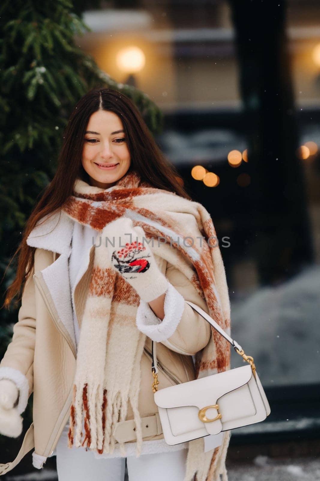 A girl with long hair in a scarf and with a white handbag walks down the street in winter by Lobachad