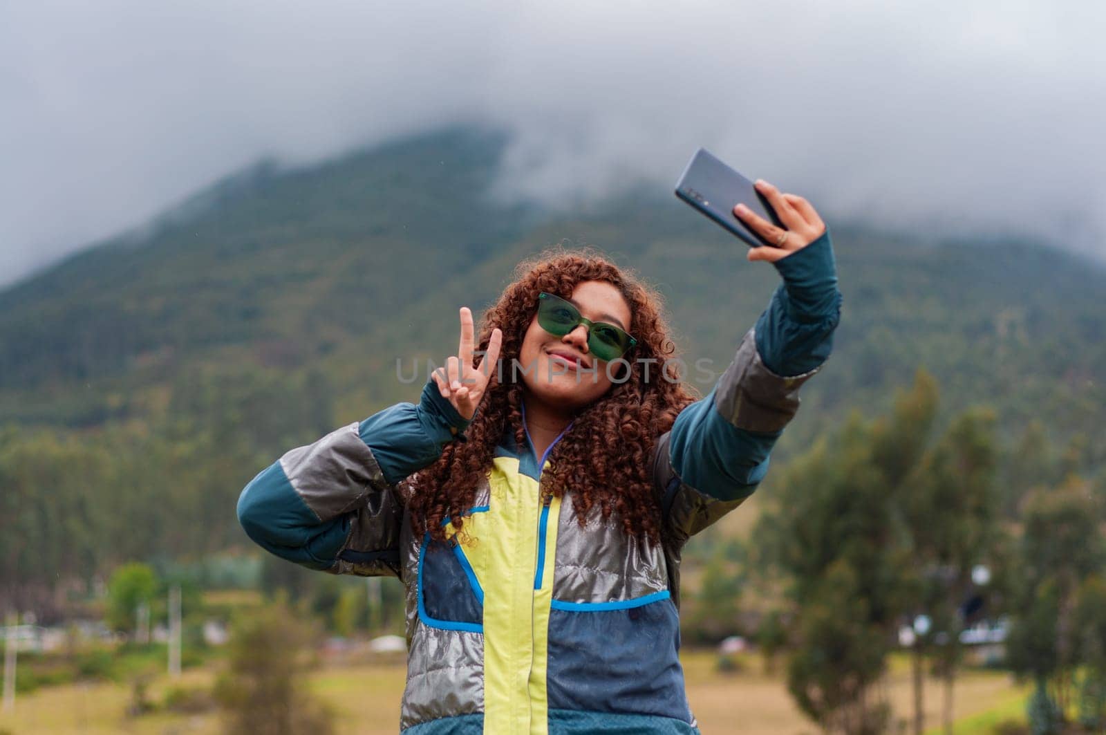 teenage rural tourism influencer from ecuador creating with had for her followers smiling and making victory sign with her fingers. by Raulmartin