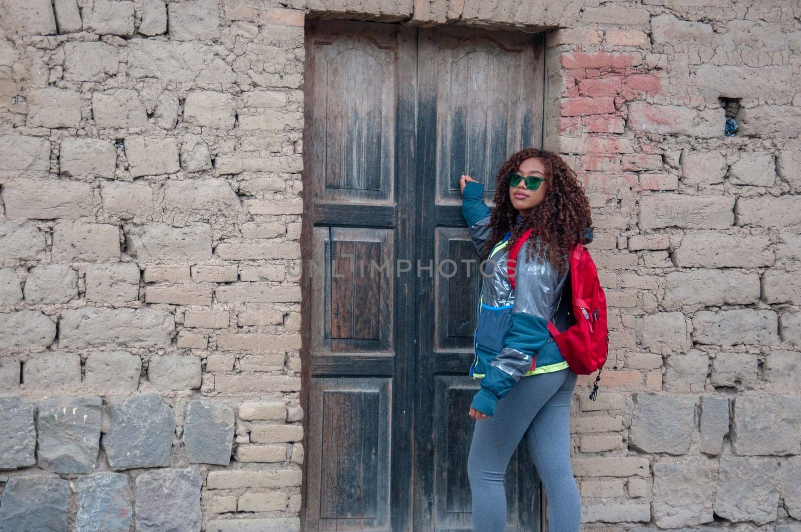 horizontal shot of a latin american woman in a rural house in south america with red backpack and mountain clothes. by Raulmartin
