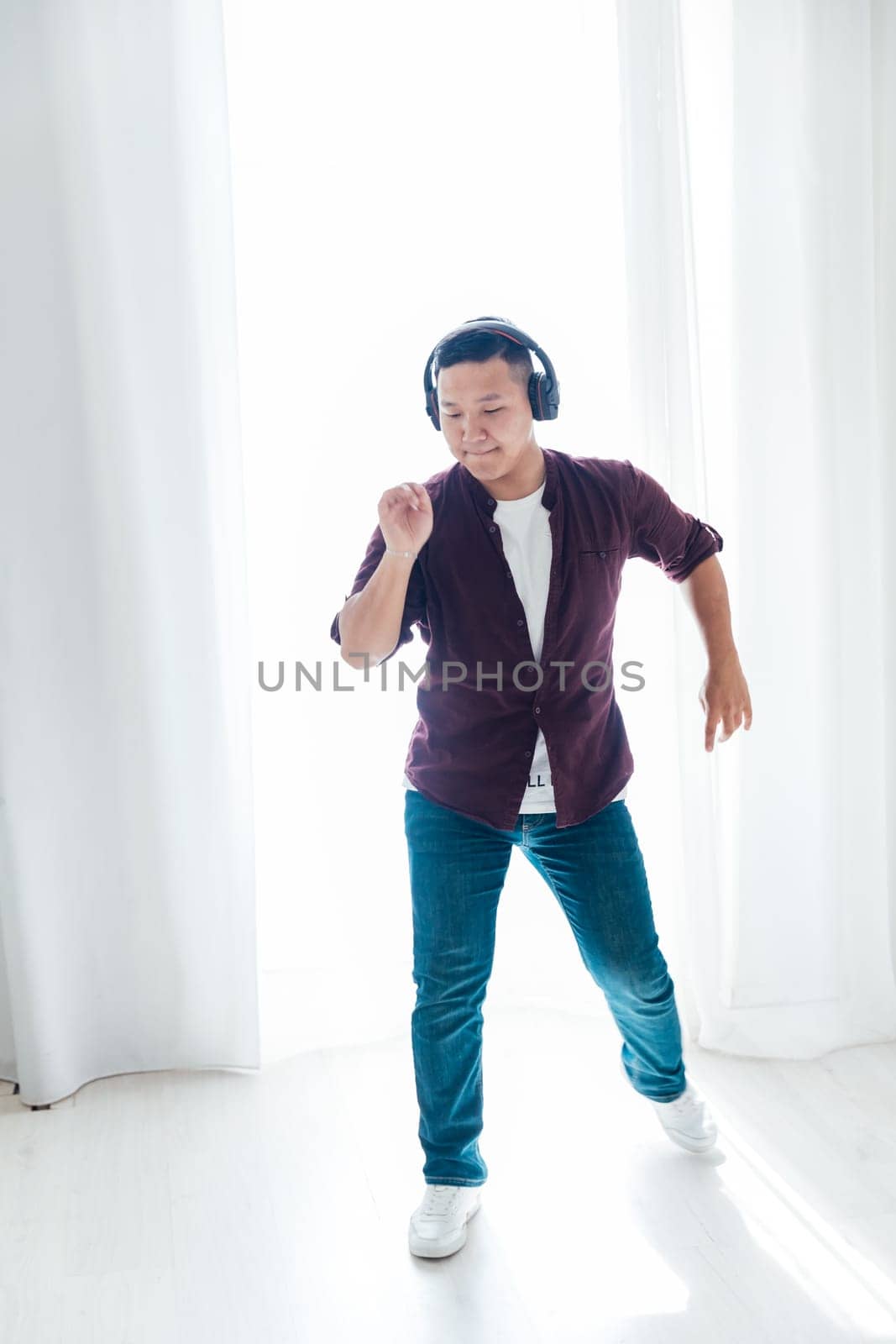 A man listens to music with headphones and dances in a bright room by Simakov