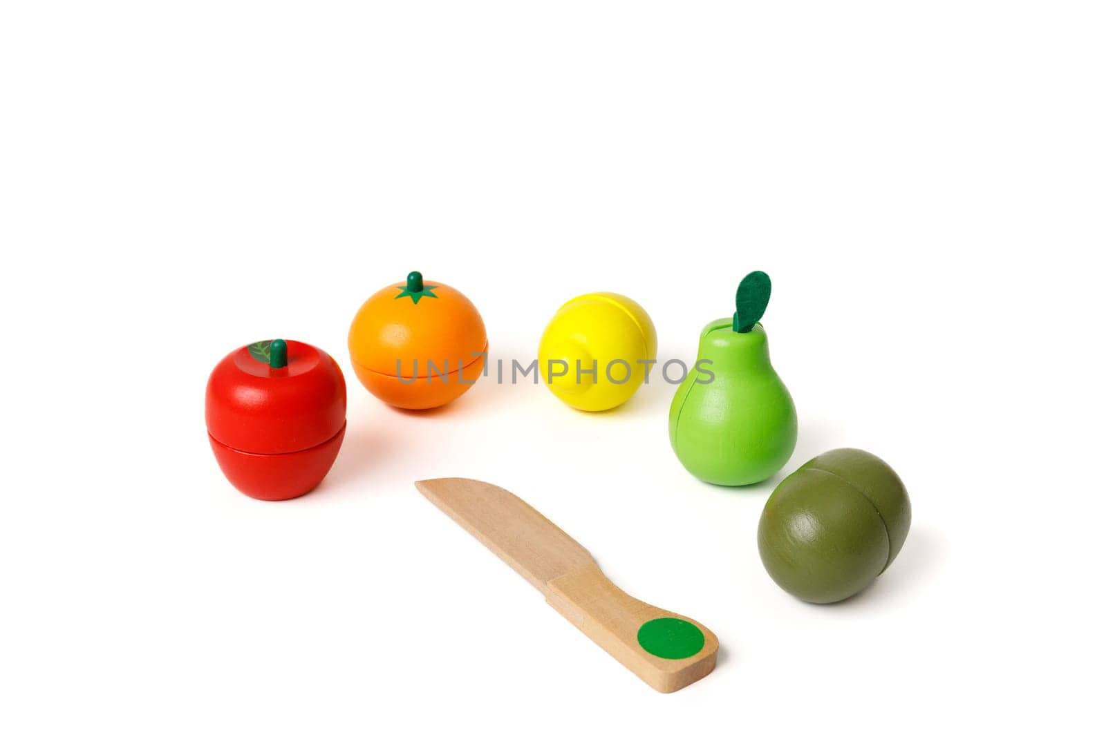 Multi-colored toys in the shape of fruits and a wooden knife for cutting these fruits. Educational games for younger preschoolers. Copy space and white background.