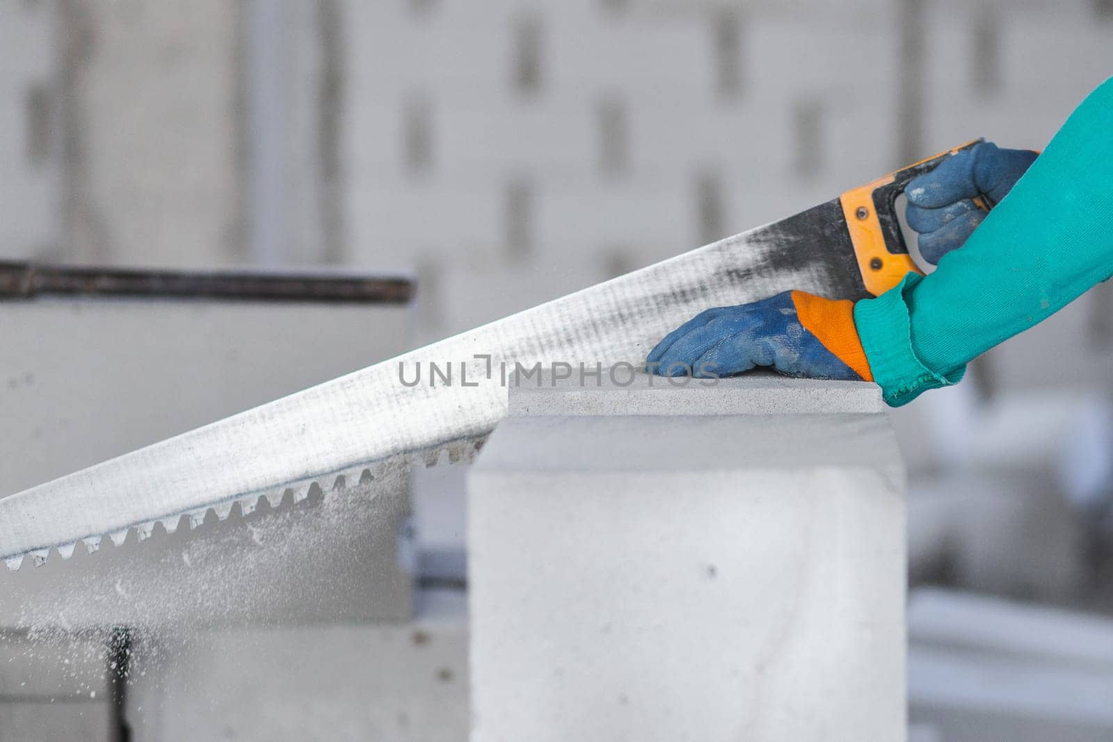A worker at a construction site saws a building block from aerated concrete at a construction site by Rom4ek
