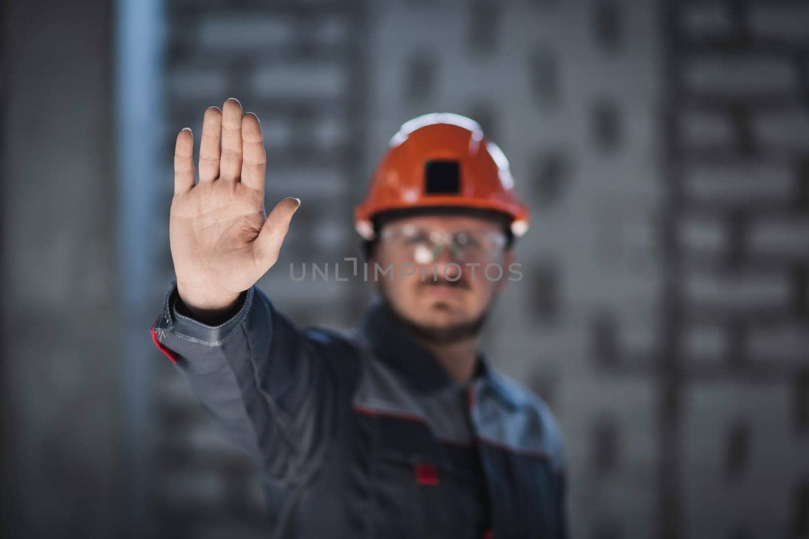 A worker in overalls and a hard hat shows an open palm demonstrating a refusal to work, a crisis in the workplace, a workers' strike by Rom4ek