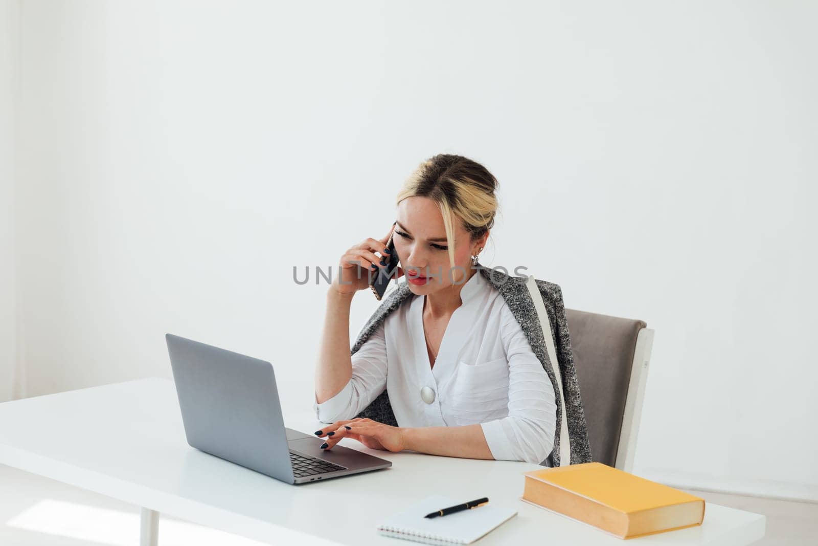 woman in office working on laptop talking on phone