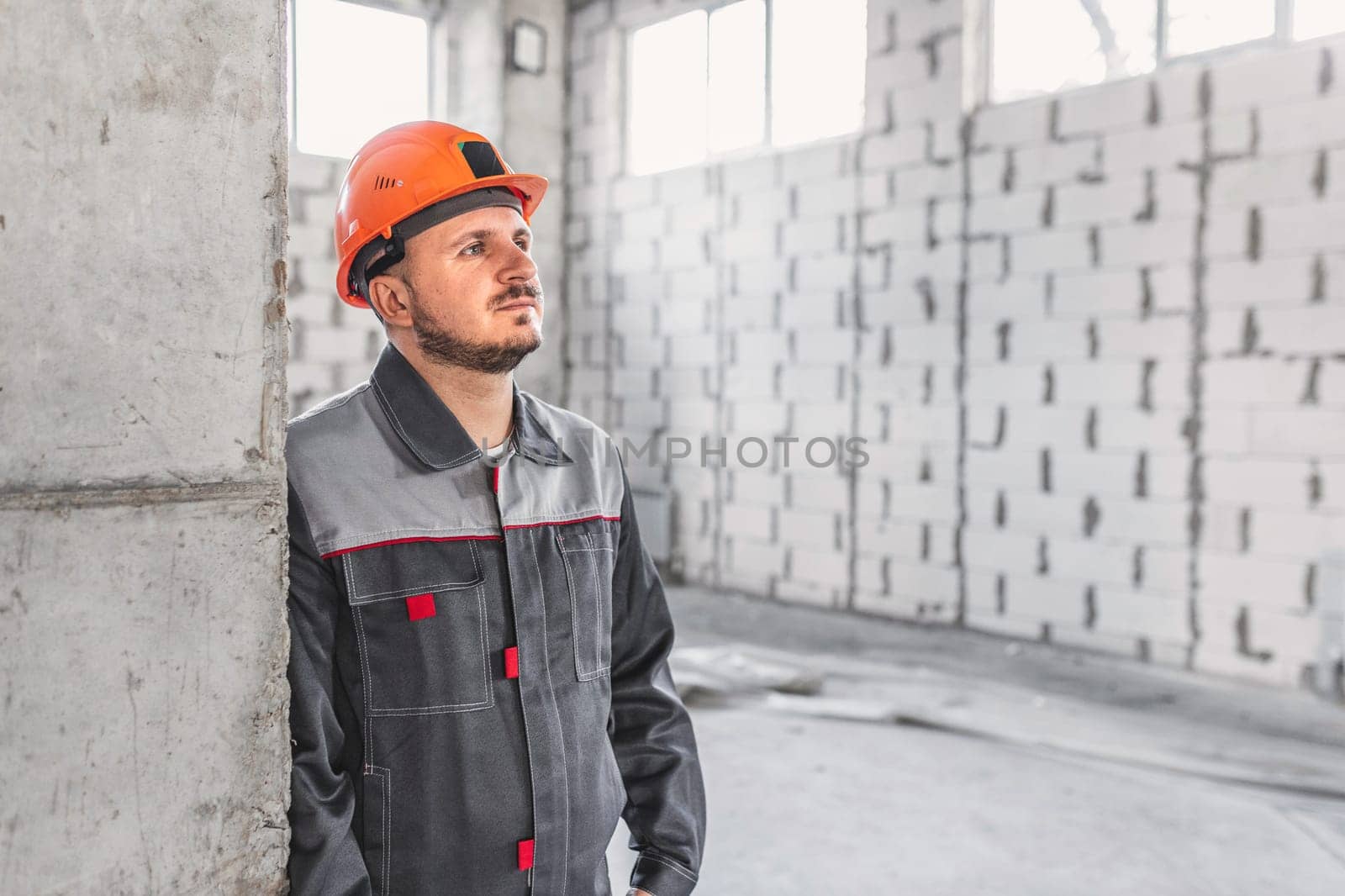 Portrait of a caucasian handyman in overalls at a construction site near a reinforced concrete column, looking to the side, copy space.