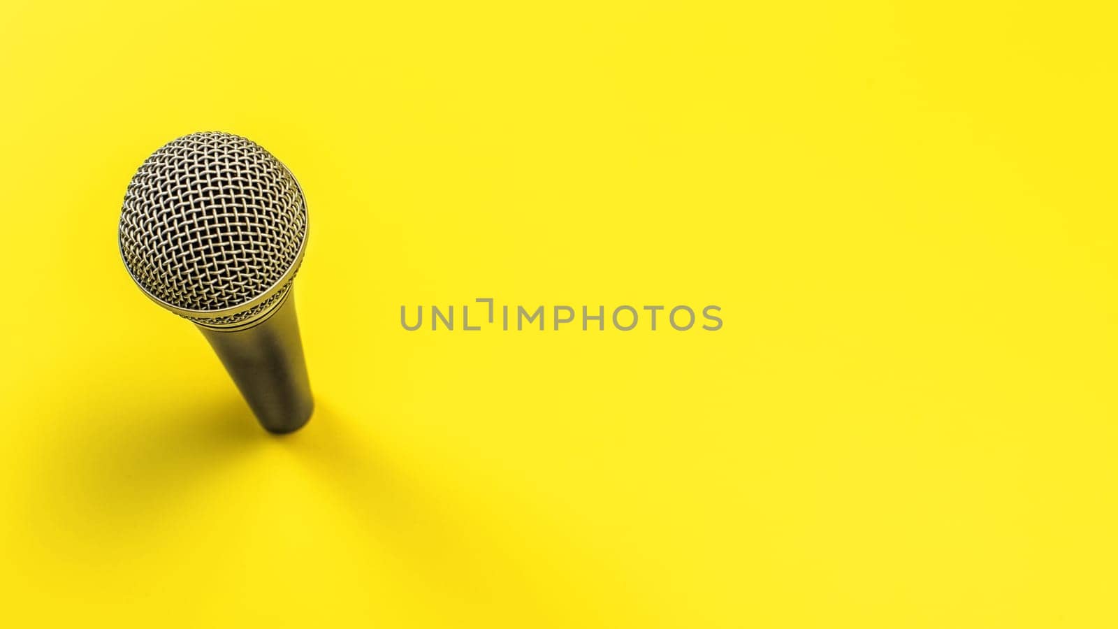 Black microphone with silver grind on yellow board, space for text right