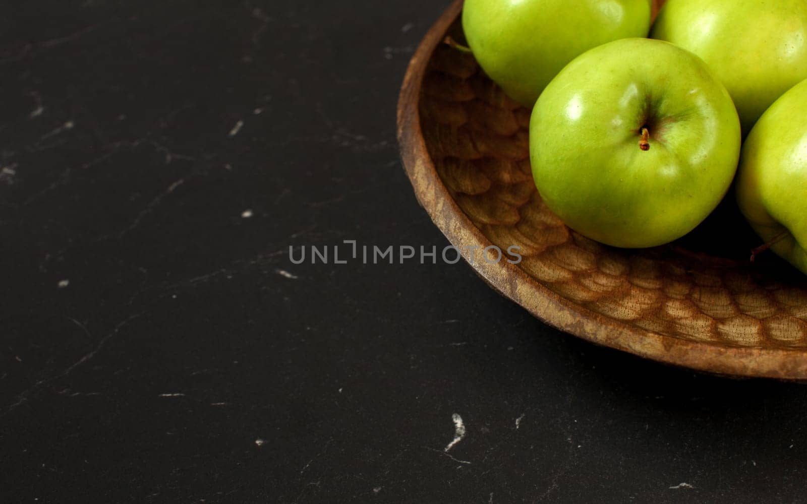 Green apples on wooden carved bowl, only part visible at black board - wide banner with space for text left