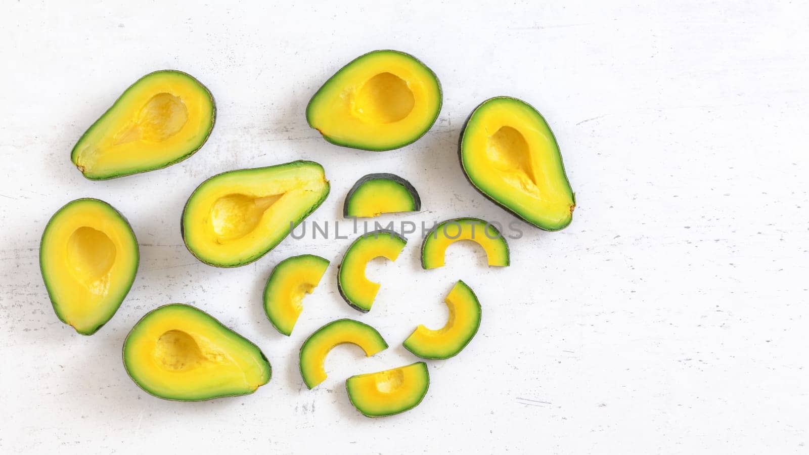 Top down view, avocado half and slices, on white working board, fruit pulp has vibrant green and yellow colour, space for text right.