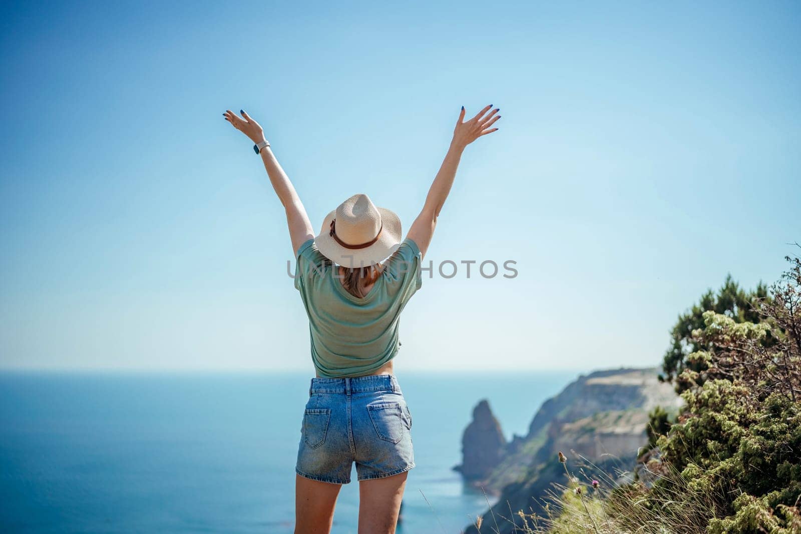Woman tourist sky sea. Happy traveller woman in hat enjoys vacation raised her hands up.