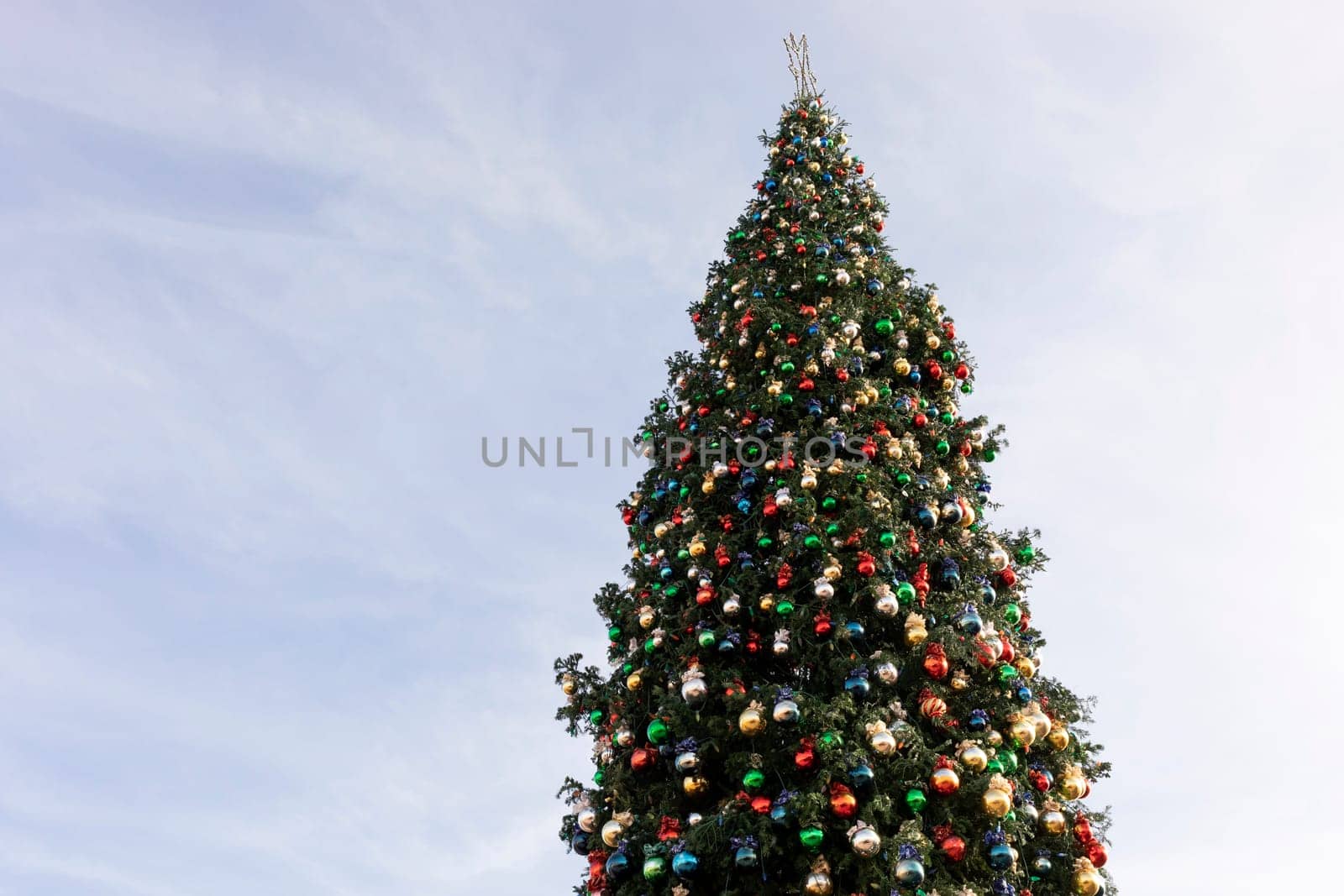 Outdoor Decorated Christmas Tree With Big Red, Golden Ball Toys And Star, Blue Sunny Sky On Background. Copy Space For Text. Horizontal Plane. New Year Elegant Pine Tree. Travel And Vacation.
