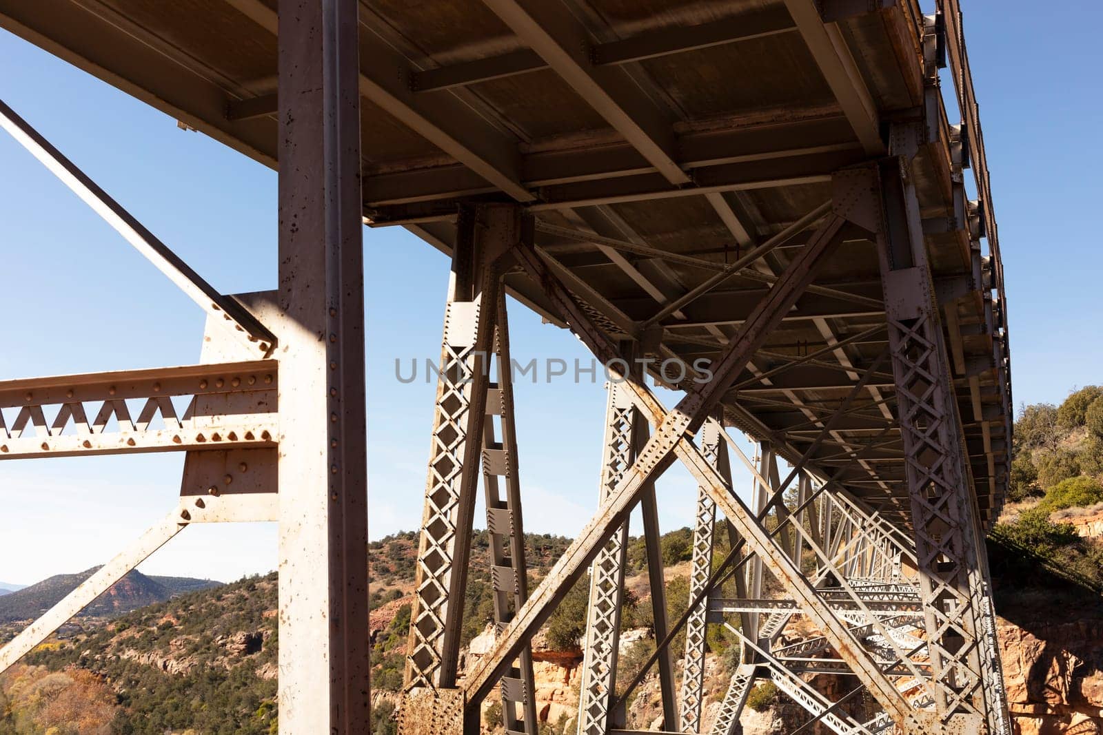 View Beneath Metal Construction Of Bridge Supports Against Blue Sky And Rocks. Rivets And Braces On Metal Beams. Midgley Bridge, Sedona Arizona. Horizontal Plane. Oak Creek Canyon, Coconino County.