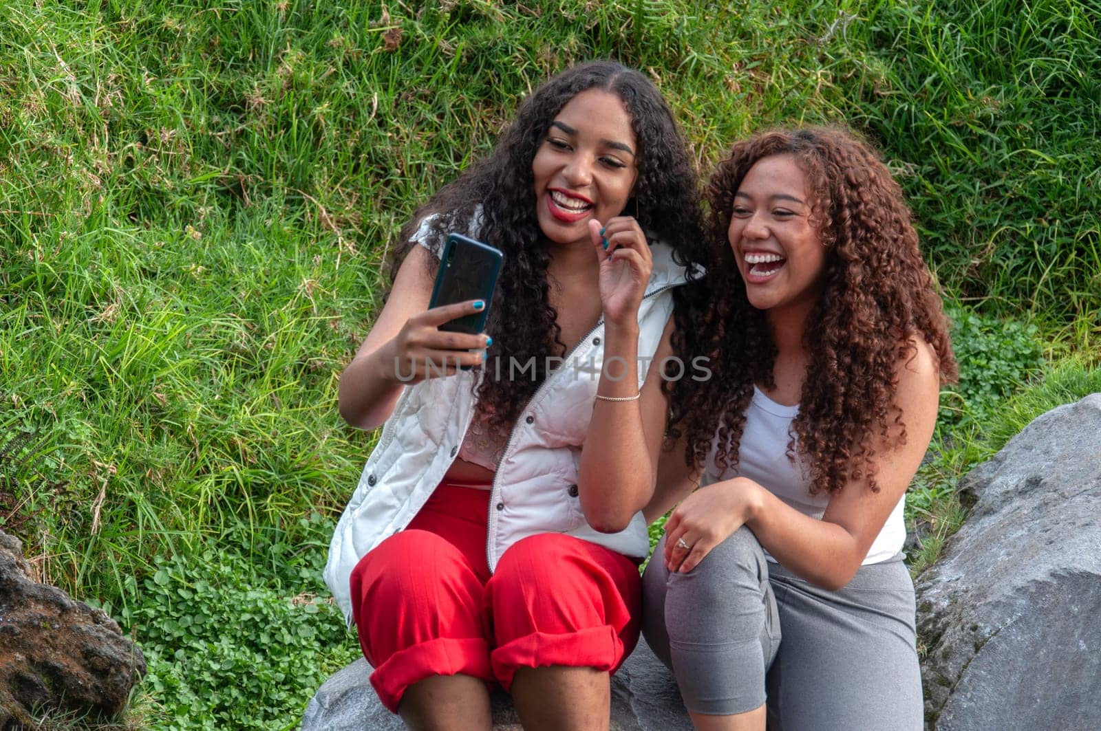 two beautiful women from latin america laughing in front of their cell phone cameras while creating content for their social networks. by Raulmartin