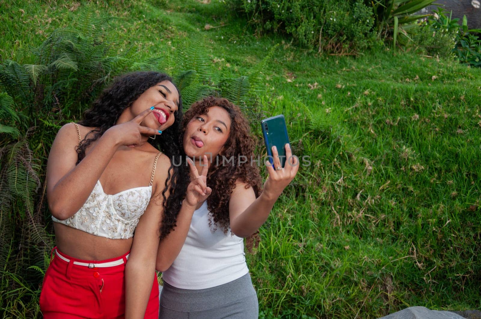 copy space of two teenagers taking a selfie with a funny expression with their tongues out and victory gestures with their fingers by Raulmartin