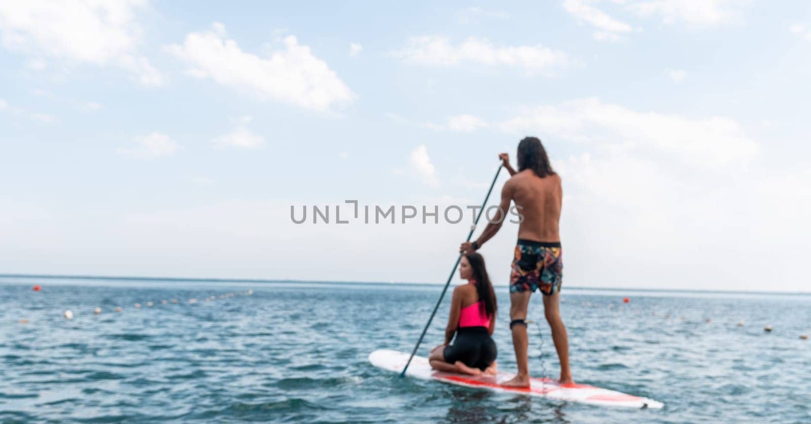 Sea woman and man on sup. Silhouette of happy young woman and man, surfing on SUP board, confident paddling through water surface. Idyllic sunset. Active lifestyle at sea or river