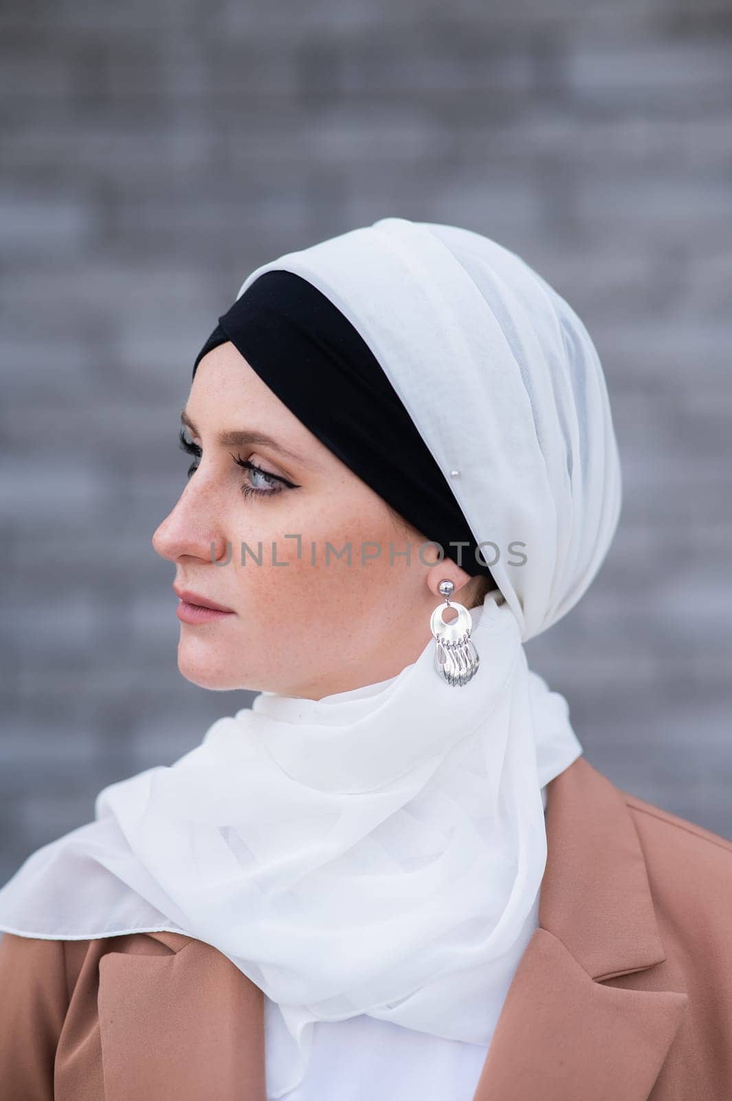 Portrait of a young blue-eyed woman in a hijab against a gray brick wall