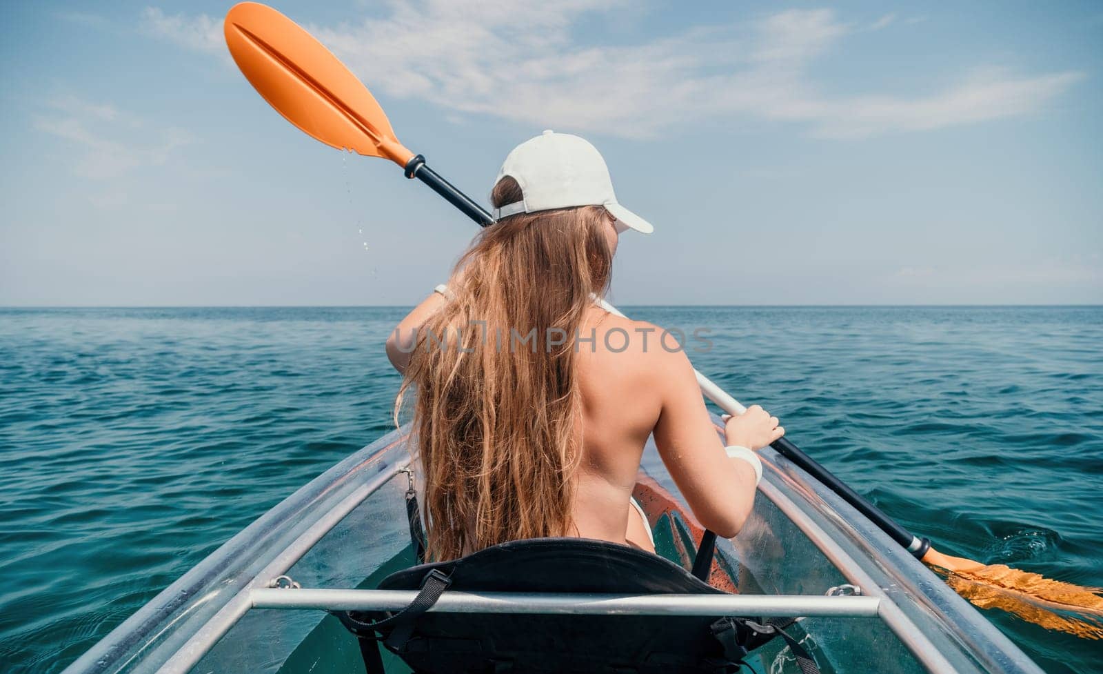 Woman in kayak back view. Happy young woman with long hair floating in transparent kayak on the crystal clear sea. Summer holiday vacation and cheerful female people having fun on the boat.