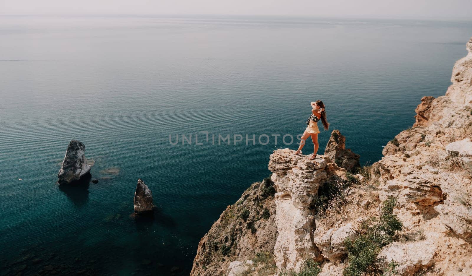 Woman travel sea. Happy tourist taking picture outdoors for memories. Woman traveler looks at the edge of the cliff on the sea bay of mountains, sharing travel adventure journey.