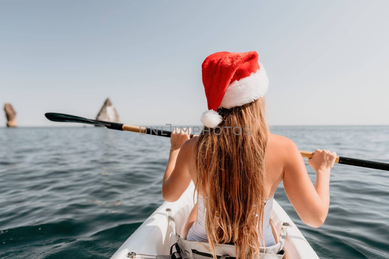 Woman in kayak back view. Happy young woman with long hair floating in transparent kayak on the crystal clear sea. Summer holiday vacation and cheerful female people relaxing having fun on the boat