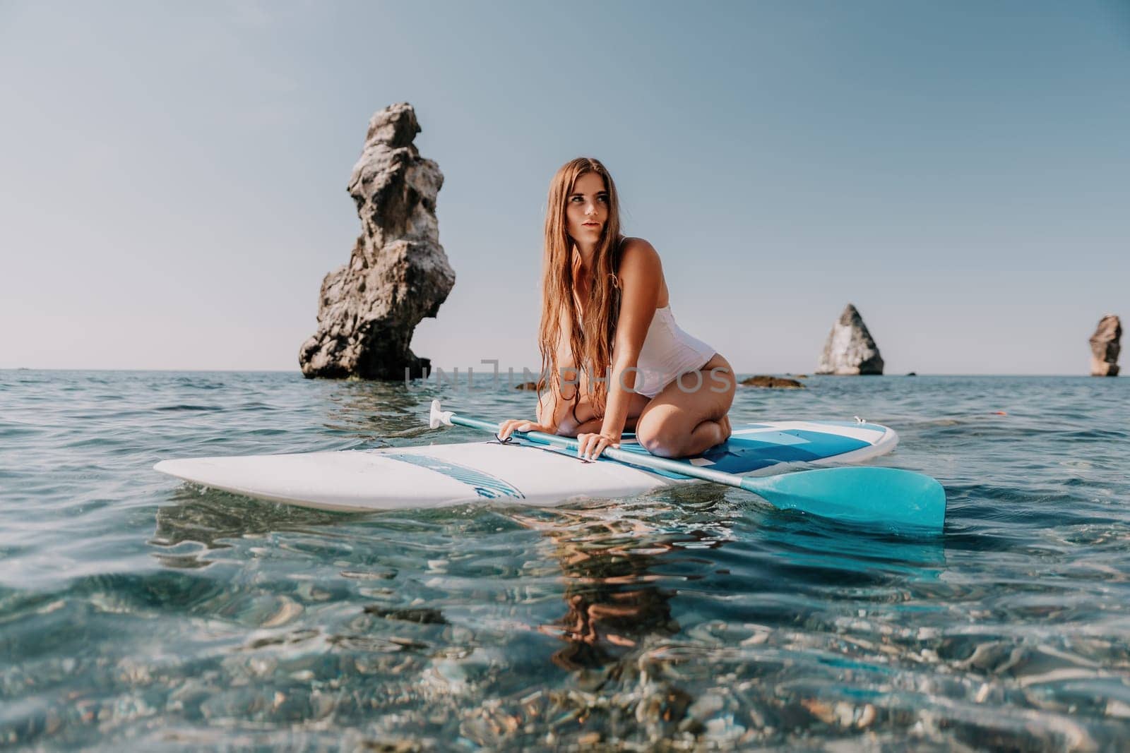 Close up shot of happy young caucasian woman looking at camera and smiling. Cute woman portrait in bikini posing on a volcanic rock high above the sea