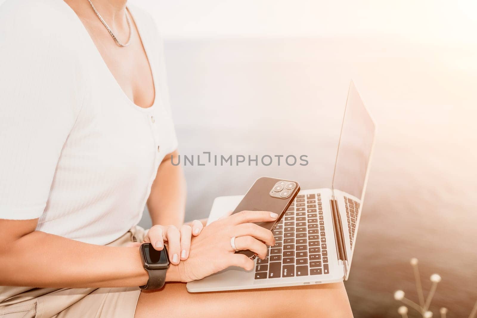 Digital nomad, Business woman working on laptop by the sea. Pretty lady typing on computer by the sea at sunset, makes a business transaction online from a distance. Freelance, remote work on vacation by panophotograph