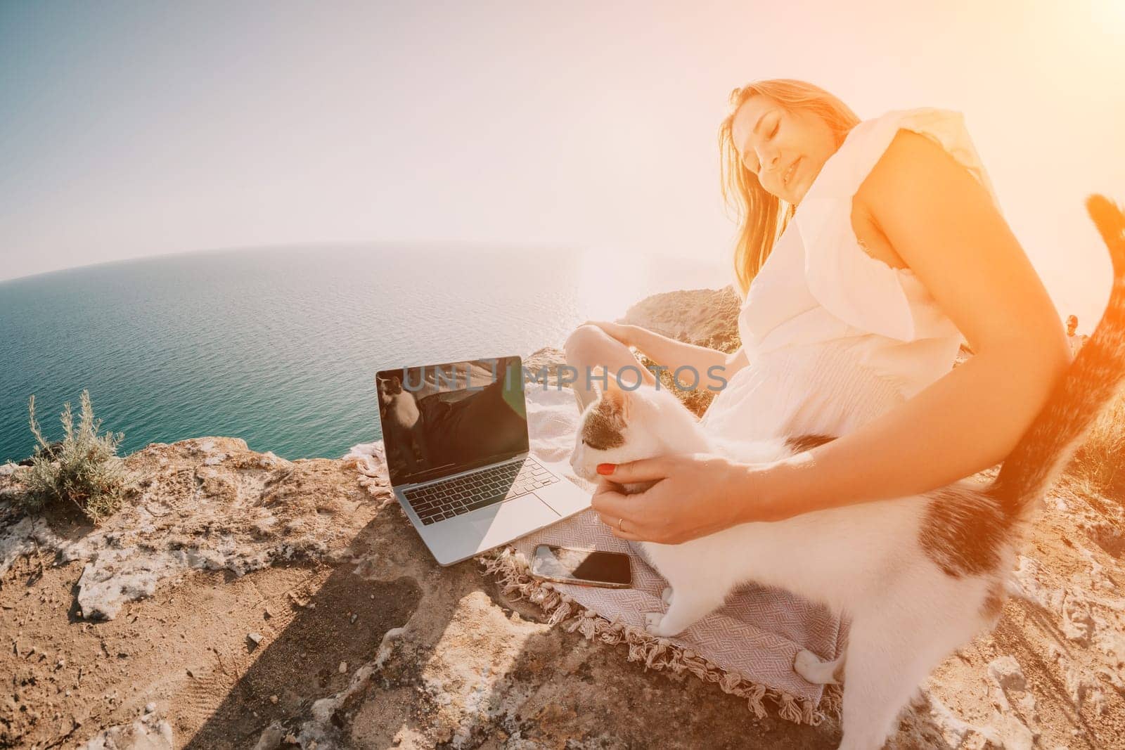 Woman sea laptop. Business woman petting cat and working on laptop by the sea. Close up on hands of pretty lady typing on computer outdoors summer day. Freelance, digital nomad and holidays concept. by panophotograph