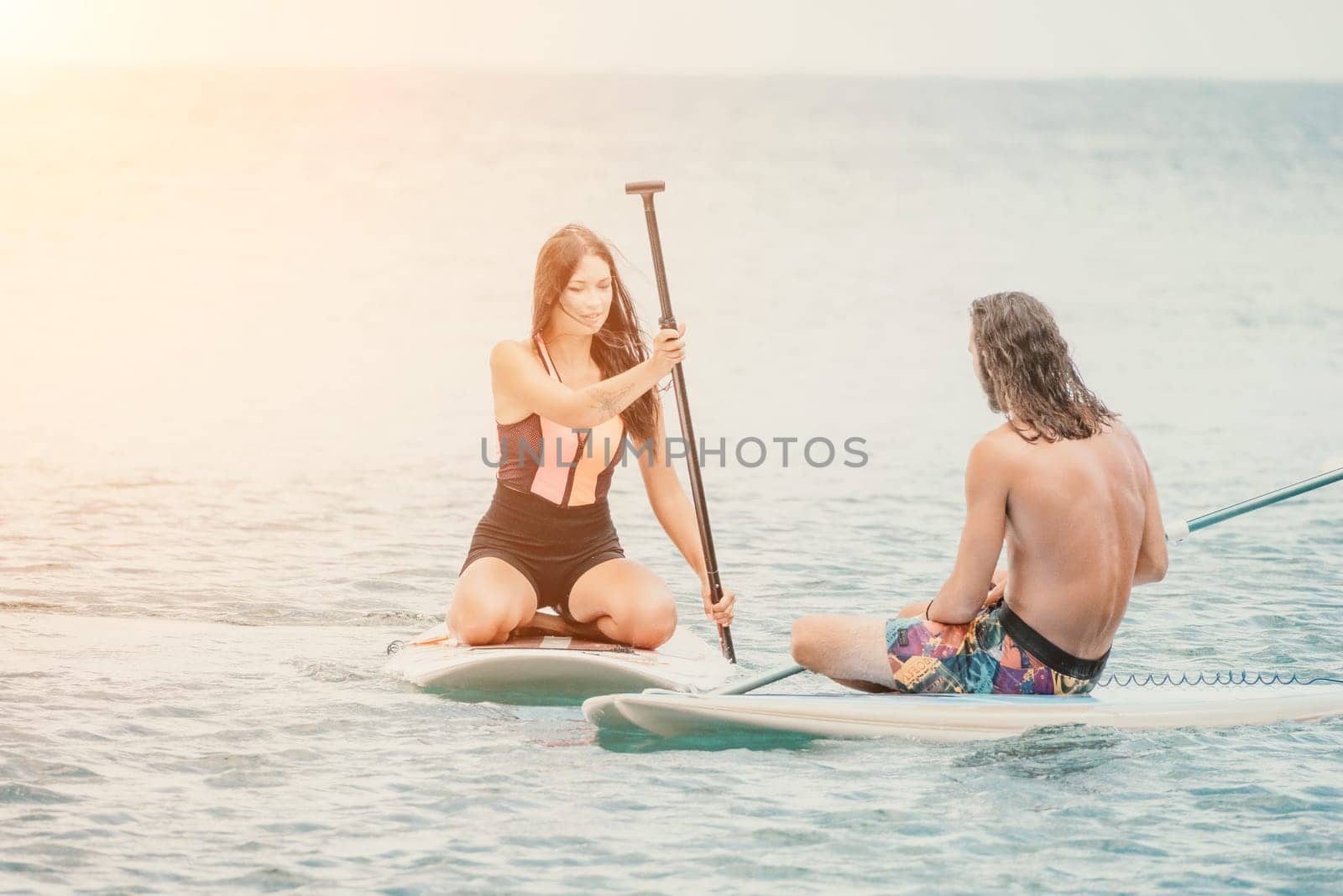 Sea woman and man on sup. Silhouette of happy young woman and man, surfing on SUP board, confident paddling through water surface. Idyllic sunset. Active lifestyle at sea or river