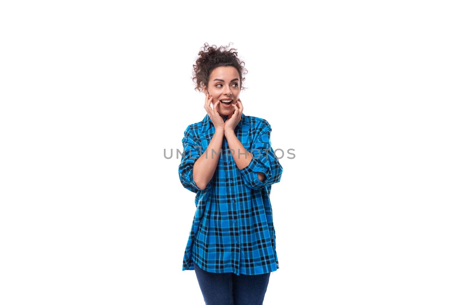 young beautiful european woman with curly hair is dressed in a blue plaid shirt with a surprised grimace on a white background by TRMK