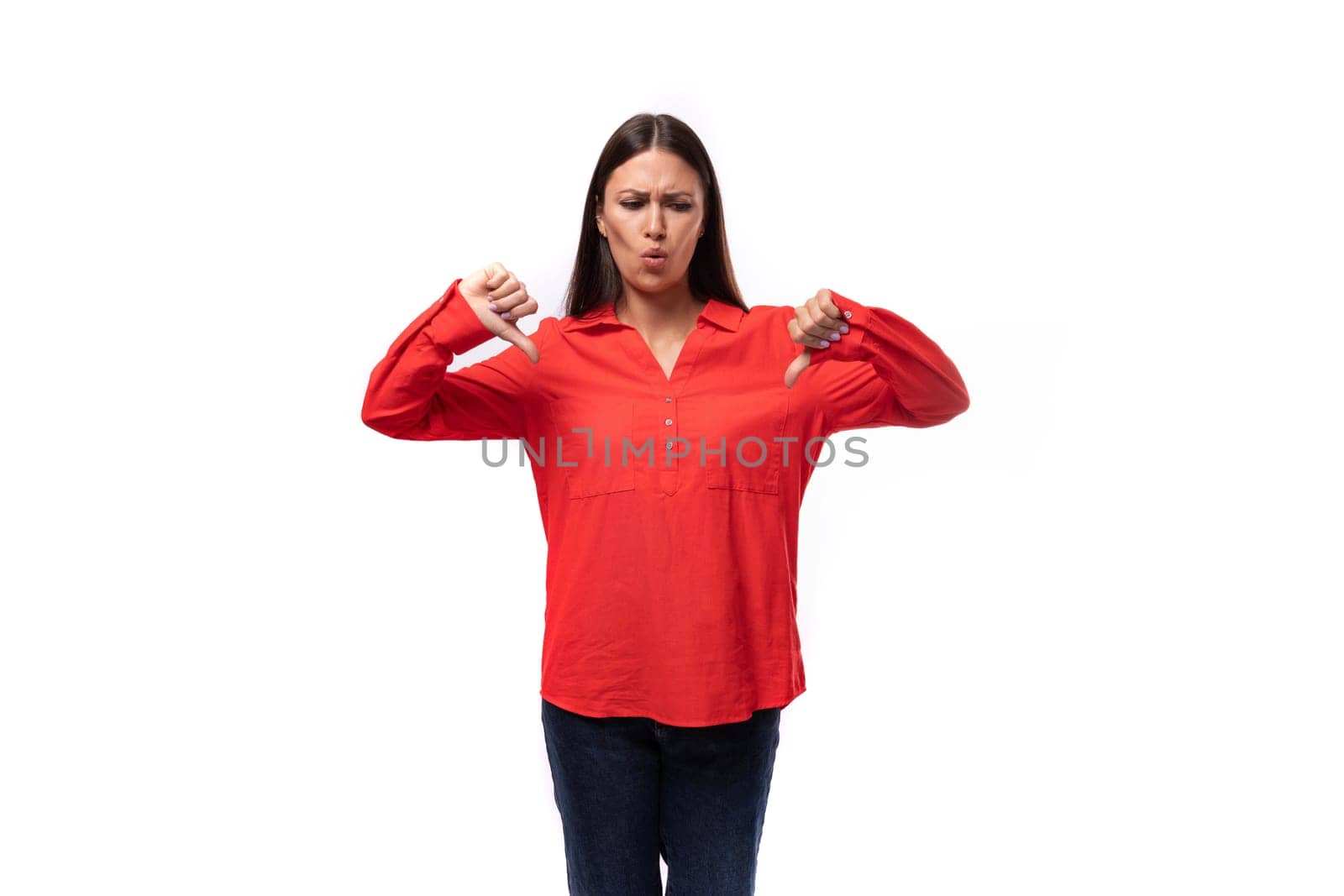 young sad brunette caucasian model woman dressed in trendy red blouse showing dislikes on white background.