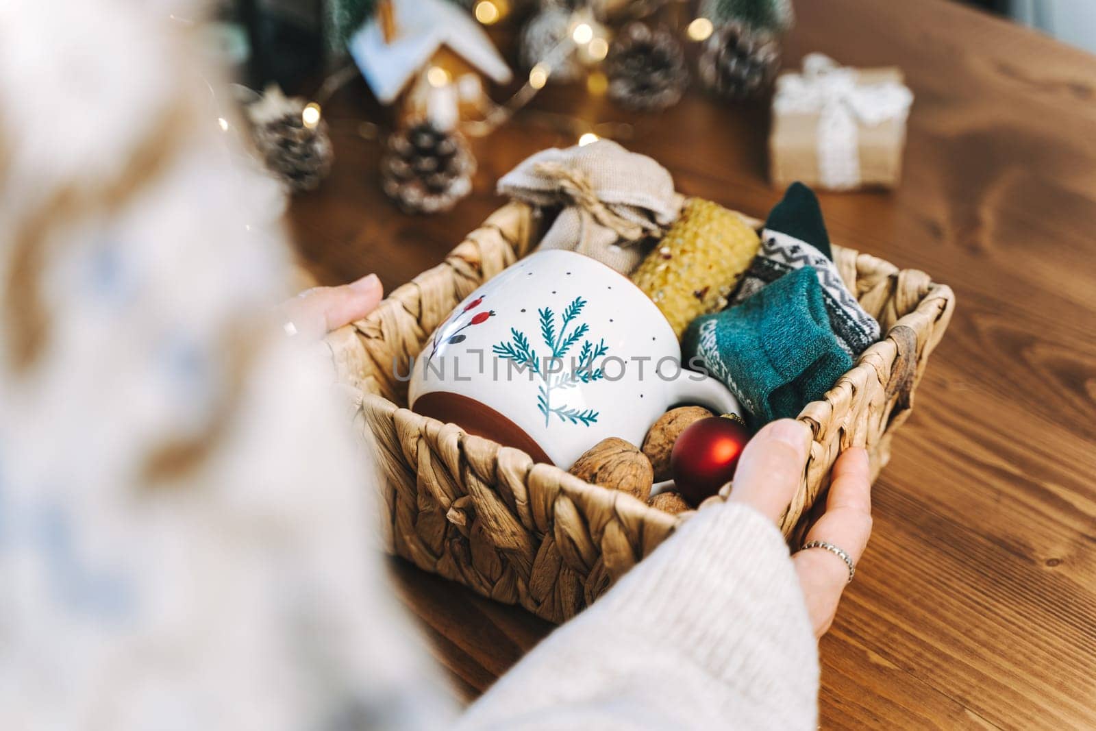 Woman s hands wrapping Christmas eco gift wicker basket, close up. Unprepared presents on wooden table with natural decor elements and items Christmas packing Concept.