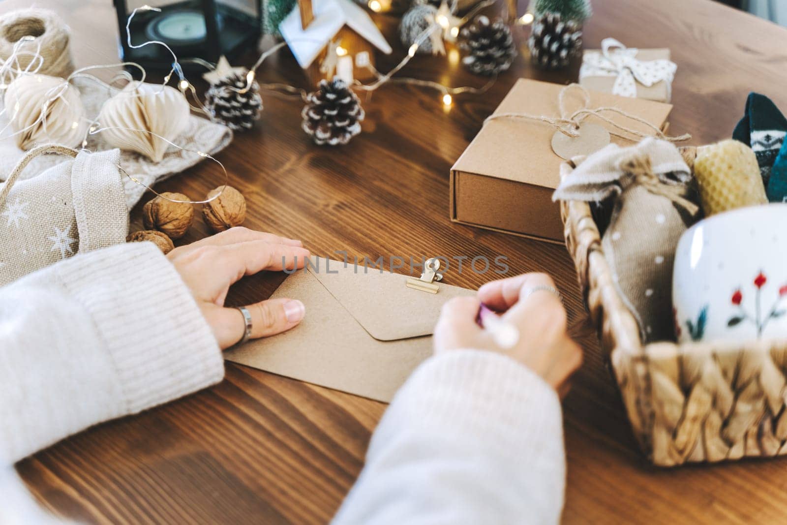 Woman s hands wrapping Christmas gift envelope, close up. Unprepared presents on white table with decor elements and items Christmas or New year DIY packing Concept.