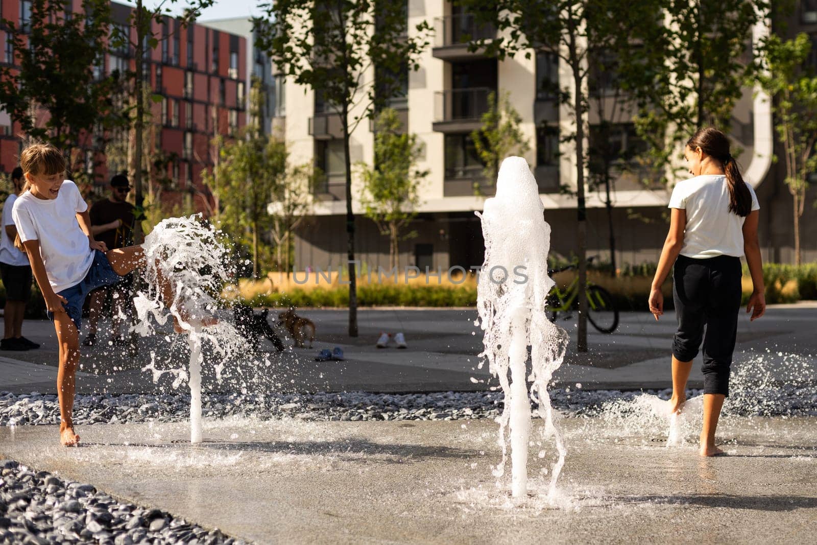 Cheerful young teen girl in city fountain, girl in wet clothes is having fun and enjoying the cool summer water, background city architecture. by Andelov13