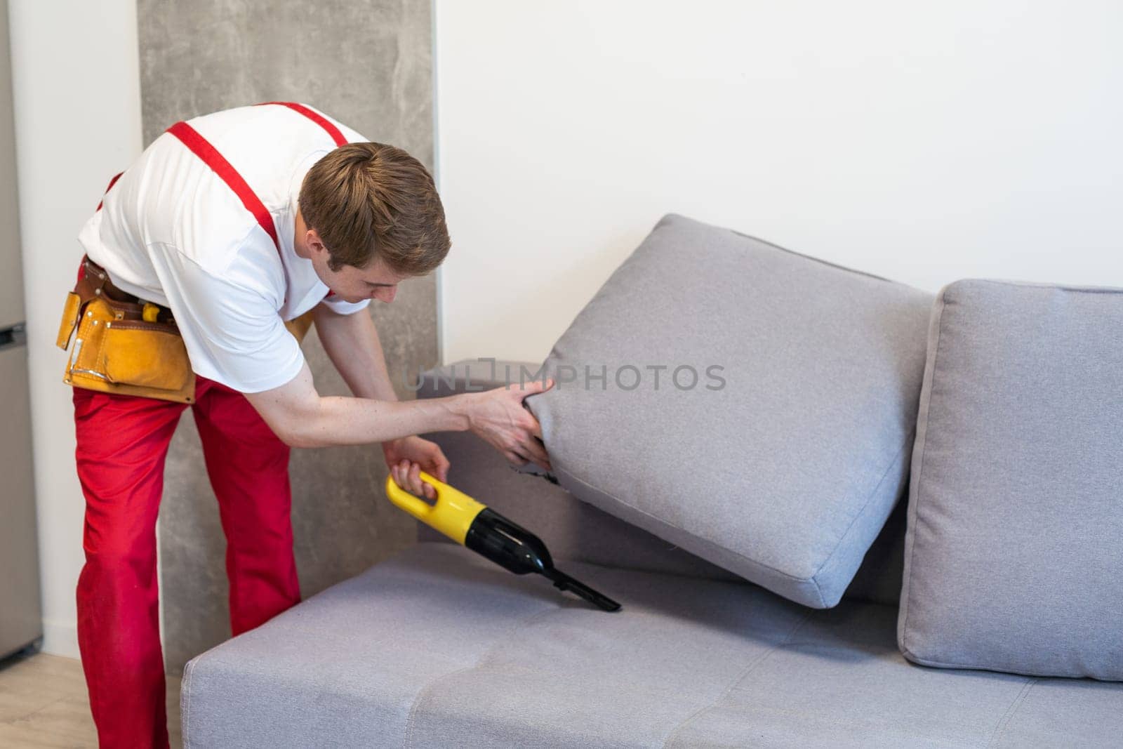 Handsome young man cleaning furniture. Process of deep furniture cleaning, removing dirt from sofa. Washing concept.