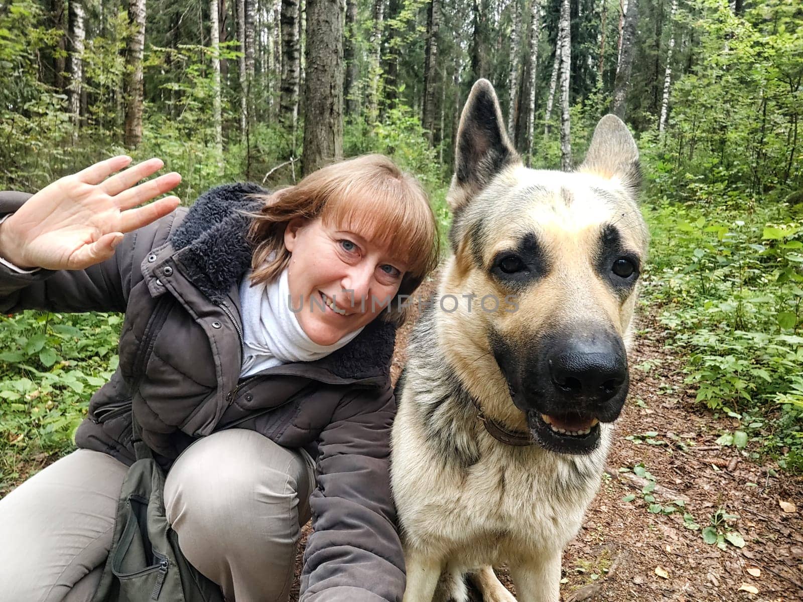 Adult girl with shepherd dog taking selfies in forest. Middle aged woman and big shepherd dog on nature. Friendship, love, communication, fun, hugs